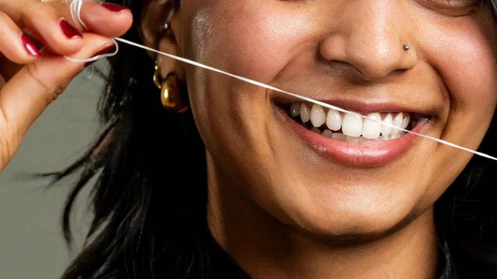 Close-up of a smiling person flossing their teeth, showing healthy gums, white teeth, and good oral hygiene.