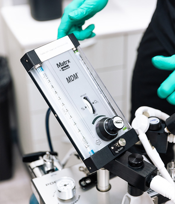 Close-up of a dental professional adjusting a nitrous oxide sedation machine with gloved hands in a modern dental clinic.