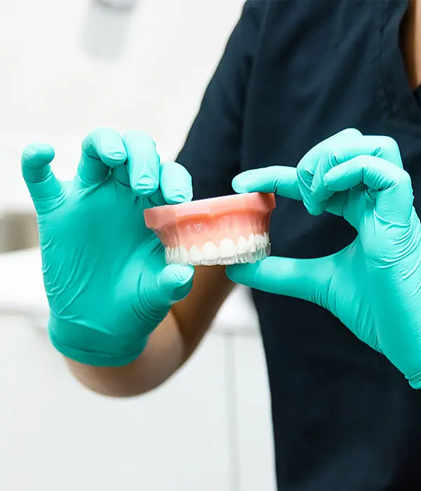 Dental professional wearing gloves holding a model of teeth fitted with clear aligners, demonstrating how Invisalign works.