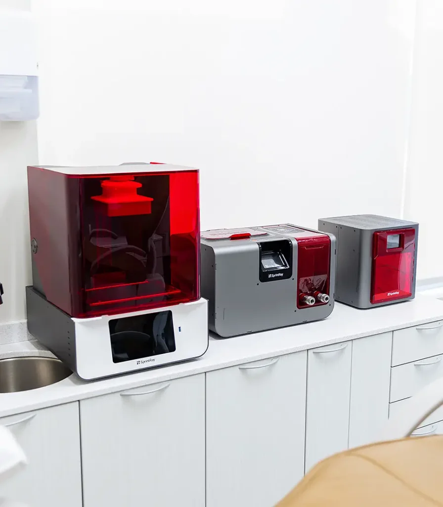 A close-up of Landmark Dental’s 3D printing machines on a countertop. The red and grey SprintRay devices are used for producing custom dental restorations in-house.